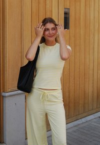 Set di abbigliamento da casa a due pezzi a strisce gialle e bianche, composto da un top aderente e pantaloni larghi con vita regolabile. Borsa tote nera.