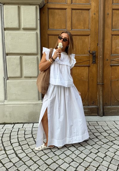 Conjunto de dos piezas blanco, con volante y falda con abertura, combinado con zapatos blancos tipo deslizables. Bolso trenzado marrón y un cono de helado en la mano.