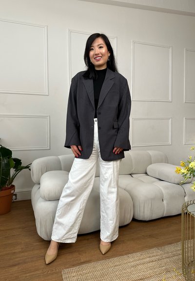 Blazer gris extragrande con solapa entallada, combinado con pantalones blancos de pierna ancha. Zapatos beige puntiagudos y top de punto negro completan el conjunto.