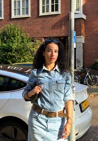 Ανοιχτό μπλε τζιν πουκάμισο με δύο τσέπες στο στήθος, συνδυασμένο με τζιν φούστα ίδιου χρώματος. Καφέ ζώνη, μαύρη τσάντα ώμου και γυαλιά ηλίου στο κεφάλι.