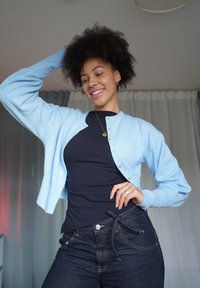 Lichtblauwe gebreide cardigan met knoopsluiting, gedragen over een zwarte T-shirt, gecombineerd met donkere denim jeans. De stof oogt zacht en gezellig.