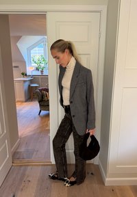 Blazer gris de lana sobre un jersey de cuello alto blanco, combinado con pantalones negros con estampado y bolso negro. El conjunto se completa con bailarinas en blanco y negro.