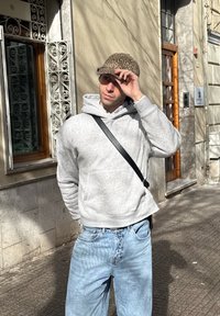 Felpa grigia con tasca a marsupio, jeans baggy azzurri, e un cappellino marrone con stampa leopardata, dotato di una tracolla e texture dettagliate.