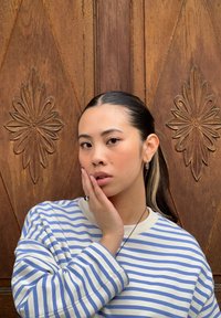 Ριγέ μπλούζα με μακριά μανίκια σε μπλε και λευκό, με υφή ξύλινου φόντου και με ανάγλυφο floral μοτίβο. Το μοντέλο ποζάρει με το χέρι στο μάγουλο.