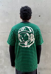 Zielono-czarna koszulka w paski z dużą białą grafiką kasku na plecach, wykonana z bawełnianej tkaniny, z krótkimi rękawami.