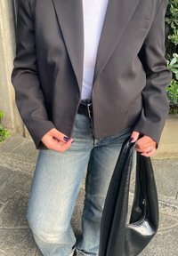 Μαύρο κομμένο σακάκι, λευκή μπλούζα, ανοιχτόχρωμο τζιν, μαύρη δερμάτινη τσάντα. Η τσάντα έχει λεία υφή και κομψό χεράκι. Επίσημη αλλά και καθημερινή εμφάνιση.