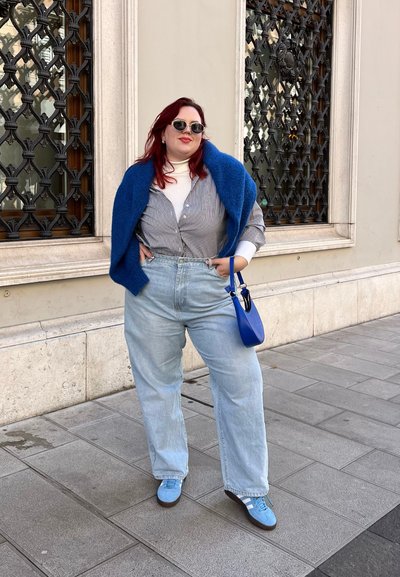 Jeans de color azul claro con una cintura alta, camisa a rayas, suéter de cuello cerrado color crema y una chalina azul. Los accesorios incluyen un pequeño bolso azul y gafas de sol.