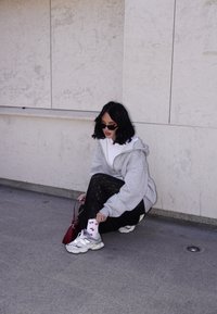Grey oversized hoodie, black lace trousers, white socks with a red fish pattern, grey trainers, and a red handbag. Neutral background and floor.