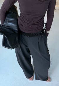 Schwarzes Langarmoberteil unter einem dunkelgrauen Blazer, kombiniert mit weit geschnittenen grauen Hosen mit seitlicher Schleife und dezenten Strukturelementen.