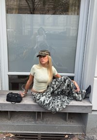 Vihreä, istuva yläosa, camo-kuosiset leveät housut ja camo-lippalakki. Asusteina musta käsilaukku ja kärkitossut.