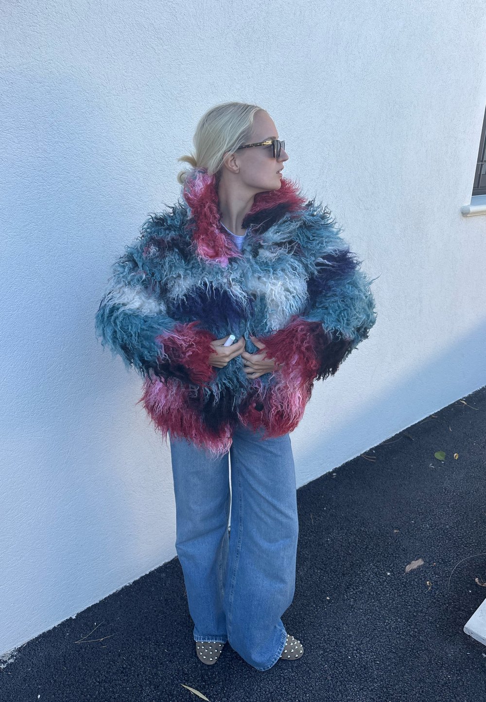 Krāsaina mākslīgās kažokādas jaka ar zaļzaļu, rozā un balta toņu sajaukumu, apjomīgu formu un teksturētu izskatu. Kopā ar gaišiem džinsa biksēm.