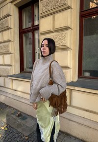 Grey knitted turtleneck sweater, fringed brown leather bag, and a light green slip skirt with lace trim. Stone background and window.