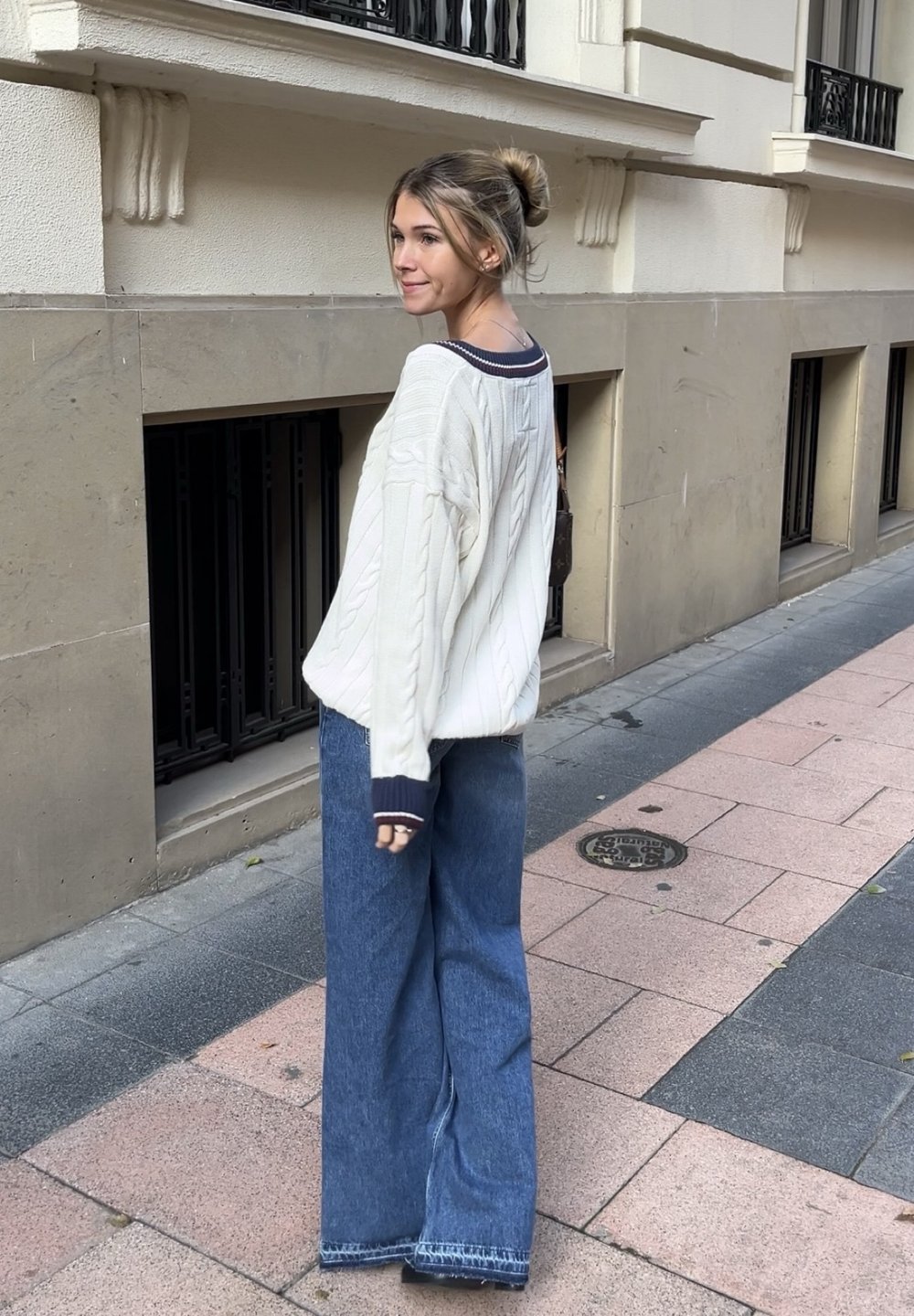 Oversized κρέμα πλεκτό πουλόβερ με ναυτικό περιθώριο, συνδυασμένο με χαλαρές μπλε τζιν παντελόνες. Υφή υφάσματος και χαλαρή εφαρμογή.