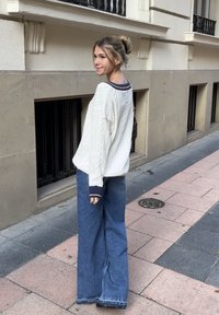 Oversized κρέμα πλεκτό πουλόβερ με ναυτικό περιθώριο, συνδυασμένο με χαλαρές μπλε τζιν παντελόνες. Υφή υφάσματος και χαλαρή εφαρμογή.