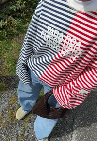 Stribet sweatshirt i rød og marineblå farver, med hvid tekst og et logo-patch. Pair med lyseblå baggy jeans og en mørk vævet taske.