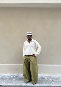 Übergroßer cremefarbener Strickpullover mit Kragen, kombiniert mit olivgrünen Hosen mit weitem Bein. Accessoires umfassen eine beige Baskenmütze und dunkle Sonnenbrille.