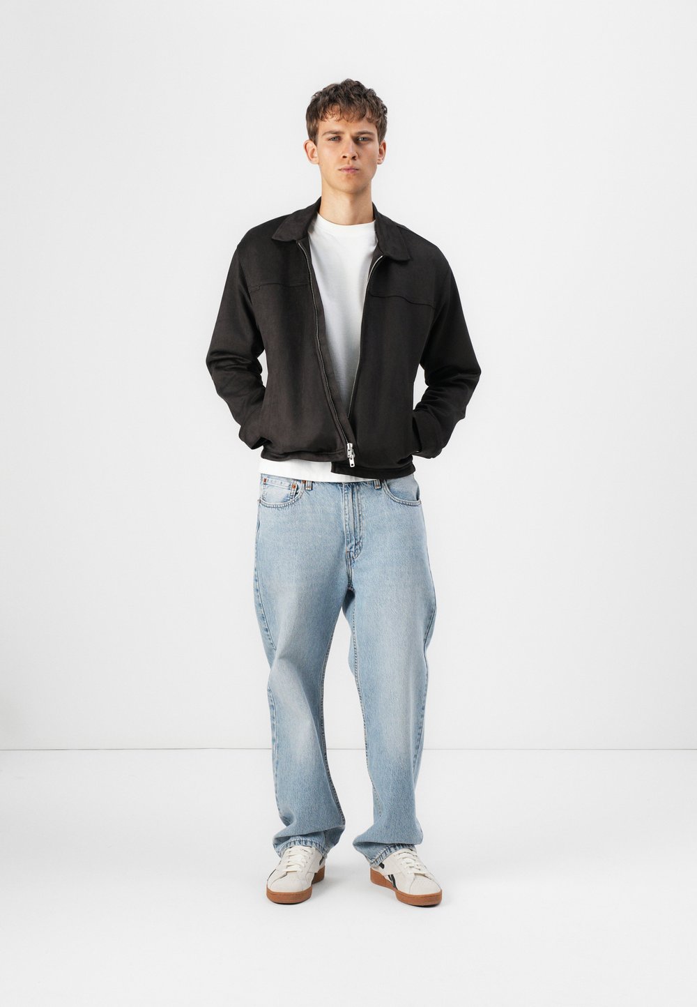 Svart zip-up jakke over en hvit t-skjorte, kombinert med lyseblå jeans og hvite sneakers. Jakken har krage og en glatt tekstur.