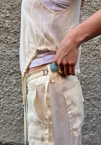 Ελεφαντόδοντο διαφανές τοπ με μαζεμένο στρίφωμα, φορεμένο πάνω από μια ριμπ μπλούζα. Ελαφρύ, ρέον ύφασμα σε συνδυασμό με κρεμ παντελόνι με μεγάλες τσέπες.