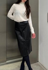 Fustă midi din piele neagră, cu un design elegant și ajustat, având detalii cu curea. Asortată cu un pulover cu guler înalt crem și ciorapi opaci negri.