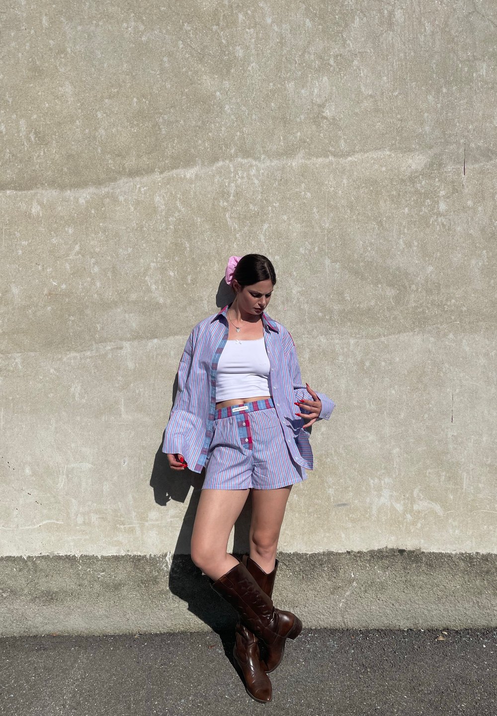 Udobna kombinacija prugaste košulje i kratkih hlača u plavoj i bijeloj boji s crvenim akcentima. Smeđi čizmasti čizmi do koljena. Lagani ružičasti materijal za kosu kao dodatak. Glatka tekstura.