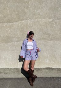 Udobna kombinacija prugaste košulje i kratkih hlača u plavoj i bijeloj boji s crvenim akcentima. Smeđi čizmasti čizmi do koljena. Lagani ružičasti materijal za kosu kao dodatak. Glatka tekstura.