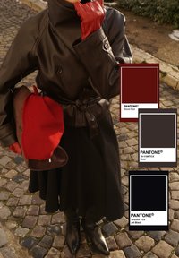Personne portant un trench-coat en cuir marron foncé, une jupe noire, des bottes noires, des gants rouges, et tenant un béret rouge sur un pavé en pierre.