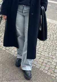 Μαύρο μακρύ παλτό, υπερμεγέθεις ανοιχτό μπλε τζιν με σκισμένα τελειώματα και χοντρές μαύρες γόβες. Λείος υφασμάτινος χαρακτήρας με αντίθετα χρώματα.