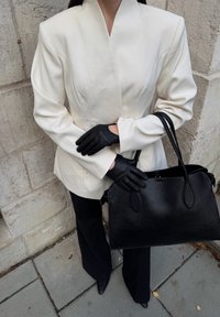 Blazer blanc ajusté avec manches longues, gants en cuir noirs et un grand sac à main noir texturé. Un pantalon noir et des chaussures pointues complètent le look.