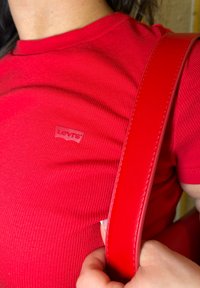 T-shirt rouge côtelé avec une petite étiquette Levi's, associé à une lanière de sac à main rouge lisse, mettant en valeur la texture et le contraste de couleurs vives.