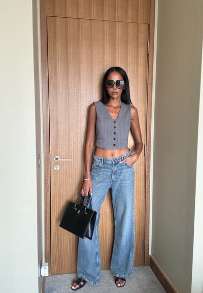 Chaleco gris corto con botones, vaqueros anchos azules, bolso negro, gafas de sol. Textura suave, diseño estructurado y acentos minimalistas.
