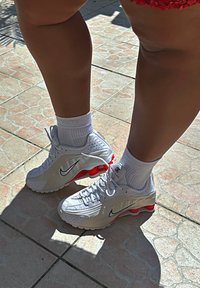 Bile Nike tenisice s crvenim akcentima, mrežasti i sintetički materijal, gumeni potplat, dizajn s vezanjem, teksturirane bočne ploče, vidljivi logo.