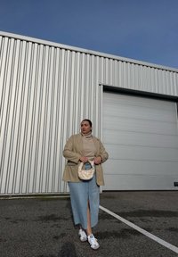 Μπεζ σακάκι πάνω από ένα ταμπά πλεκτό πουλόβερ, συνδυασμένο με μια ανοιχτού μπλε τζιν φούστα με μπροστινή σχισμή, λευκά αθλητικά παπούτσια και ένα πλεκτό λευκό τσάντα.