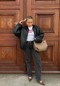 Μαύρο δερμάτινο μπουφάν bomber πάνω από λευκό μπλουζάκι με κόκκινο κείμενο, σκούρο γκρι φαρδύ τζιν παντελόνι, καφέ τσάντα και γόβες με λεοπάρ σχέδιο.