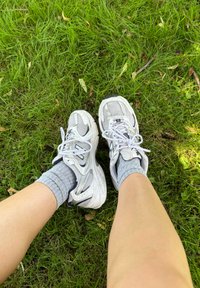 Weiße Sportsneaker mit Mesh-Details, grauen Akzenten und weißen Schnürsenkeln, kombiniert mit grauen Socken, die auf grünem Gras liegen.