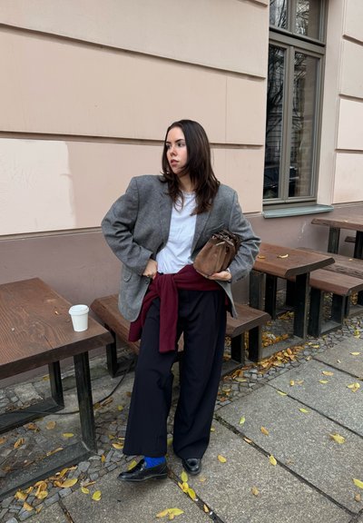 Blazer de cuadros gris, camiseta blanca, pantalones anchos de pierna oscura, suéter granate anudado a la cintura, bolso marrón, calcetines azules, zapatos negros.