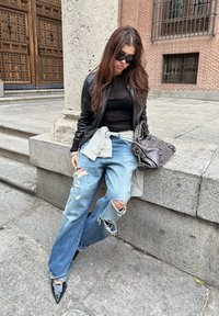 Črna usnjena jakna, prozorna črna majica, ohlapne svetlo modre jeans hlače s strganinami. Dodatki vključujejo sivo karo srajco, vezano okoli pasu, in temno torbico.