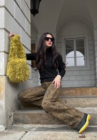 Čierny rolák, hnedé zvieracie vzorované rozšírené nohavice, masívne čierno-žlté topánky a chlpatá olivovo zelená taška. Sedí na kamenných schodoch.