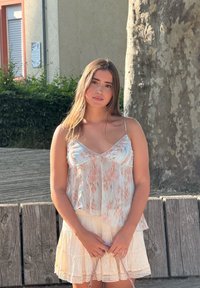 Lättviktig, ärmlös topp i pastellfärger med en flödande design. Matchad med en tärningsformad, krämfärgad kjol med spetsdetaljer vid fållen.