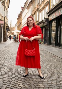 Vestido rojo de manga larga con lunares texturizados, cintura ceñida y falda acampanada. Combinado con un bolso acolchado rojo y zapatos negros.