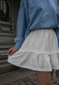 Felpa oversize blu chiaro abbinata a una gonna bianca in pizzo con volant, caratterizzata da un motivo a zigzag e orlo scallop.