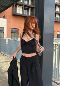 Crna skraćena majica s uvrnutim prednjim dijelom, u paru s labavim crnim hlačama. Dodaci uključuju uzorkovanu kravatu i višeslojne ogrlice.