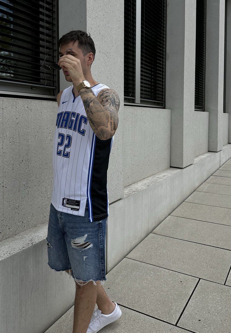 Vit baskettröja med blå och svarta detaljer, prydlig vertikala ränder och nummer 22. Bärs ihop med slitna denimshorts och vita sneakers.