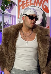 Brauner Kunstfellmantel über einem weißen Tanktop, geschichtete silberne Ketten mit Kreuzanhängern, schwarze Sonnenbrille und ein weißes Bandana.