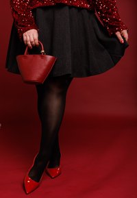 Bolso de cuero rojo con diseño curvo y asa corta. Falda negra plisada, medias negras transparentes y tacones rojos brillantes de punta afilada.