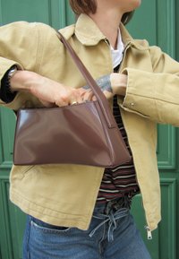 Borsa a mano in pelle patent marrone con un design strutturato e manico corto. Presenta una superficie liscia e angoli netti, che si abbinano perfettamente all'abbigliamento casual.