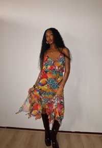 Maxi dress with vibrant floral and butterfly patterns in multiple colors. Lightweight fabric, ruffled hem, strappy design, paired with knee-high brown boots.