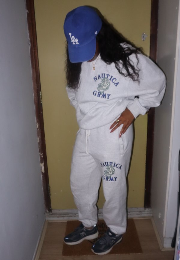 Graue Sweatpants und Sweatshirt mit dem Text "Nautica GRMY" in Blau. Getragen mit einer blauen Mütze und navyfarbenen Sneakers, die ein schlichtes und strukturiertes Design aufweisen.