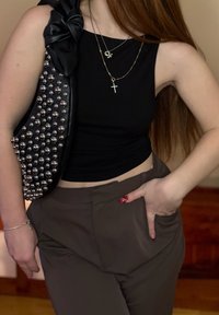 Haut court noir avec un ourlet froncé, associé à un pantalon marron taille haute. Les accessoires comprennent des colliers dorés superposés et un sac noir clouté.