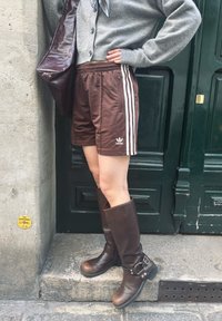 Rudos Adidas šortai su baltais šonų dryžiais, derinami su rudos odos kelnių batais iki kelių. Pilkas kardiganas ir ruda odos rankinė užbaigia įvaizdį.