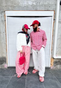 Casal com roupas coordenadas em xadrez vermelho e branco. Um usa um topo felpudo branco e calças estampadas, enquanto o outro veste uma camisa xadrez e calças.